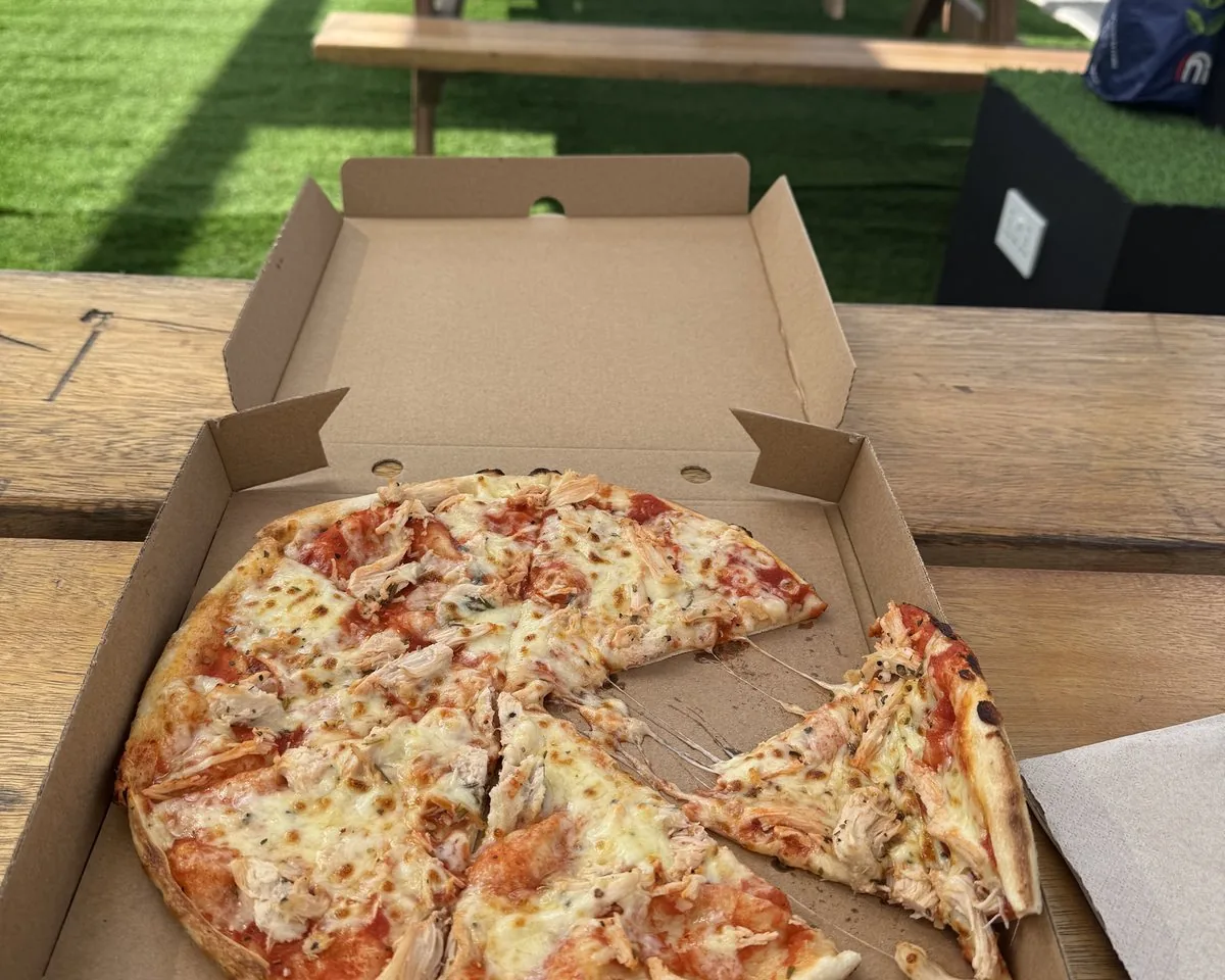Hộp pizza trên bàn gỗ ngoài sân, bữa trưa trong khu hội chợ Gulfood 2026